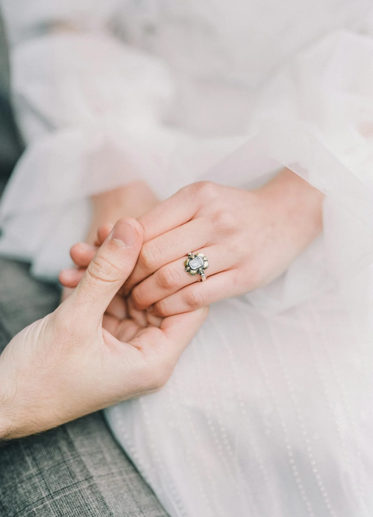 Image featuring a close-up of two hands gently holding each other, highlighting a vintage-style engagement ring.