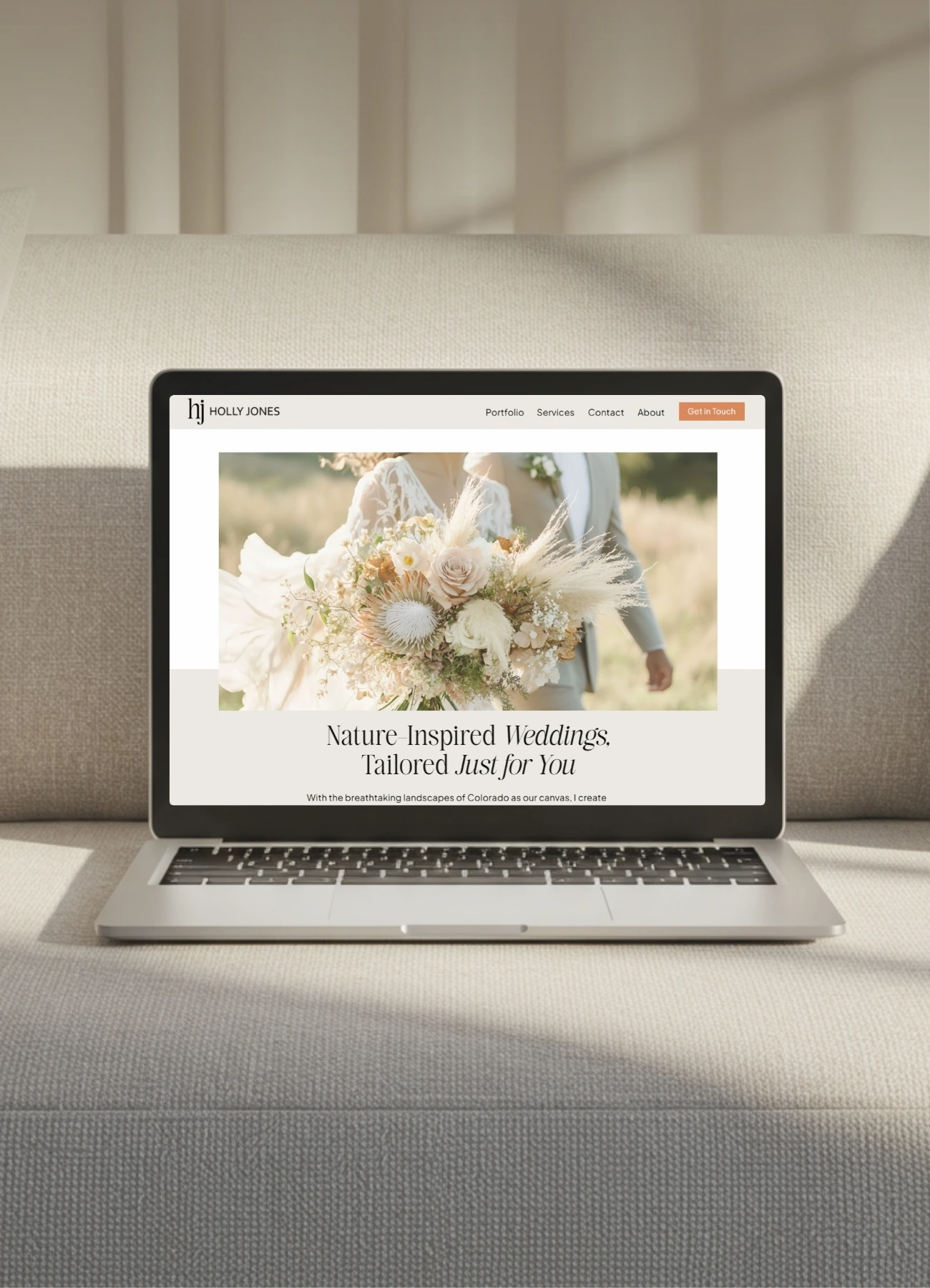 A laptop displaying a wedding website with elegant serif typography and a soft, neutral color palette sits on a beige couch.